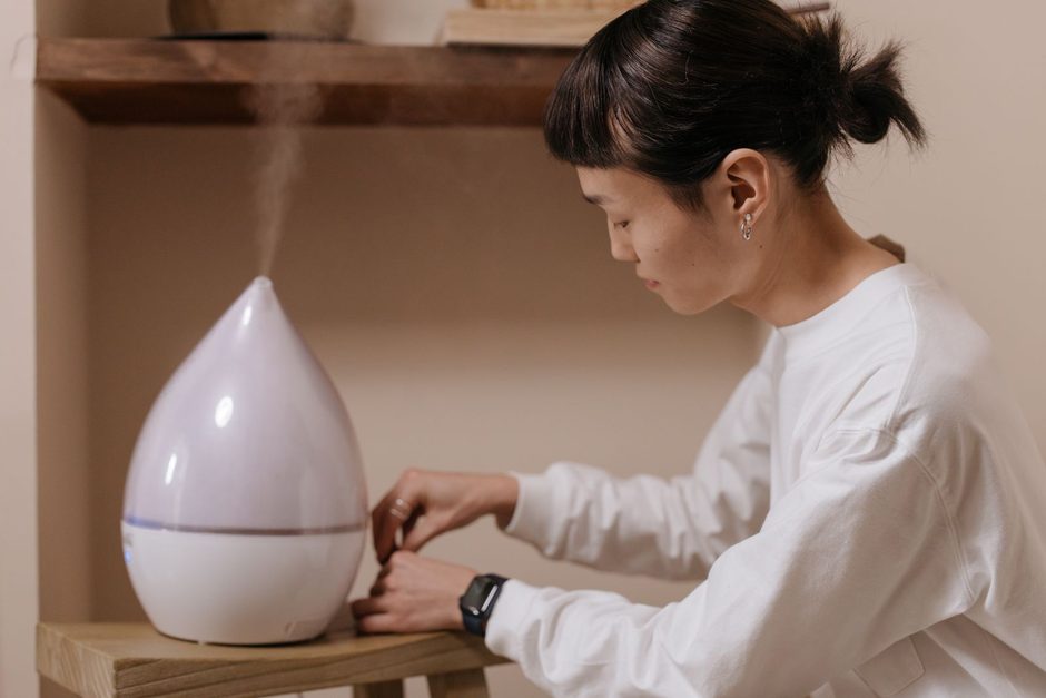 Woman setting up a white humidifier on a wooden table at home to control indoor humidity. Photo by cottonbro studio on Pexels